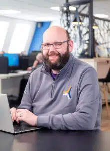 Mike, a company director, sitting at a desk in the SEP2 office using his laptop smiling at the camera